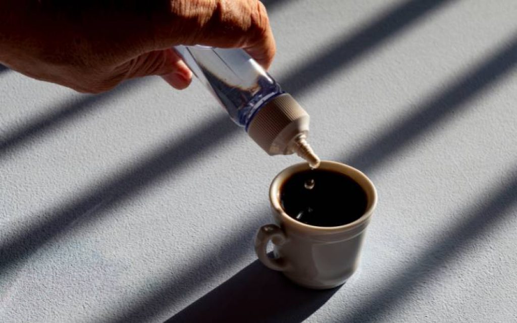 Pessoa adoçando xícara de café com adoçante