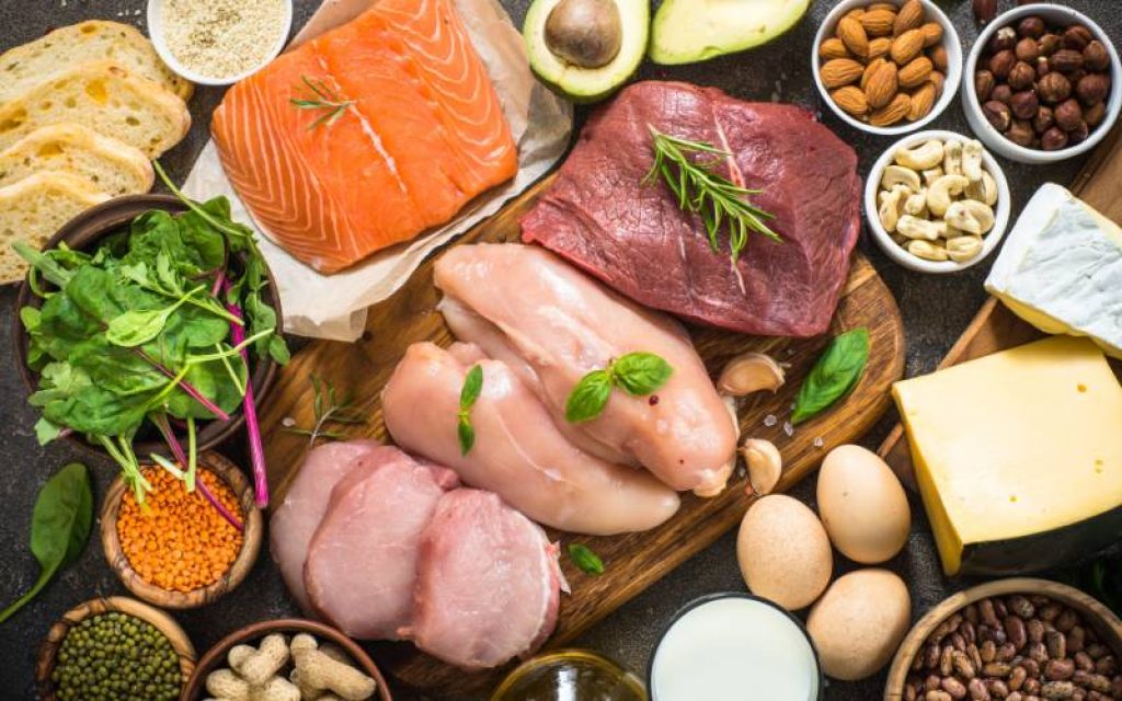 Uma mesa cheia de alimentos proteicos como carne vermelha, frango, salmão, ovos e queijos