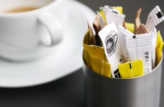 Xícara de café em um pires, ao lado de um pote com alguns adoçantes
